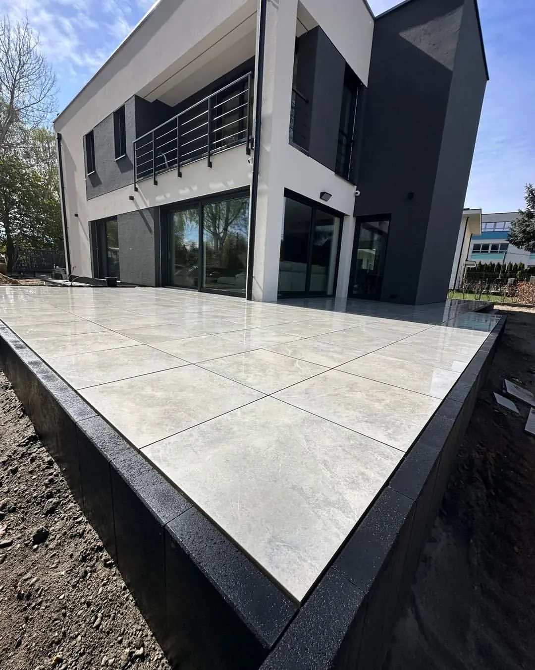 Krawędź tarasu z gresu 60x60 wykończona ciemnymi palisadami montowanymi pionowo