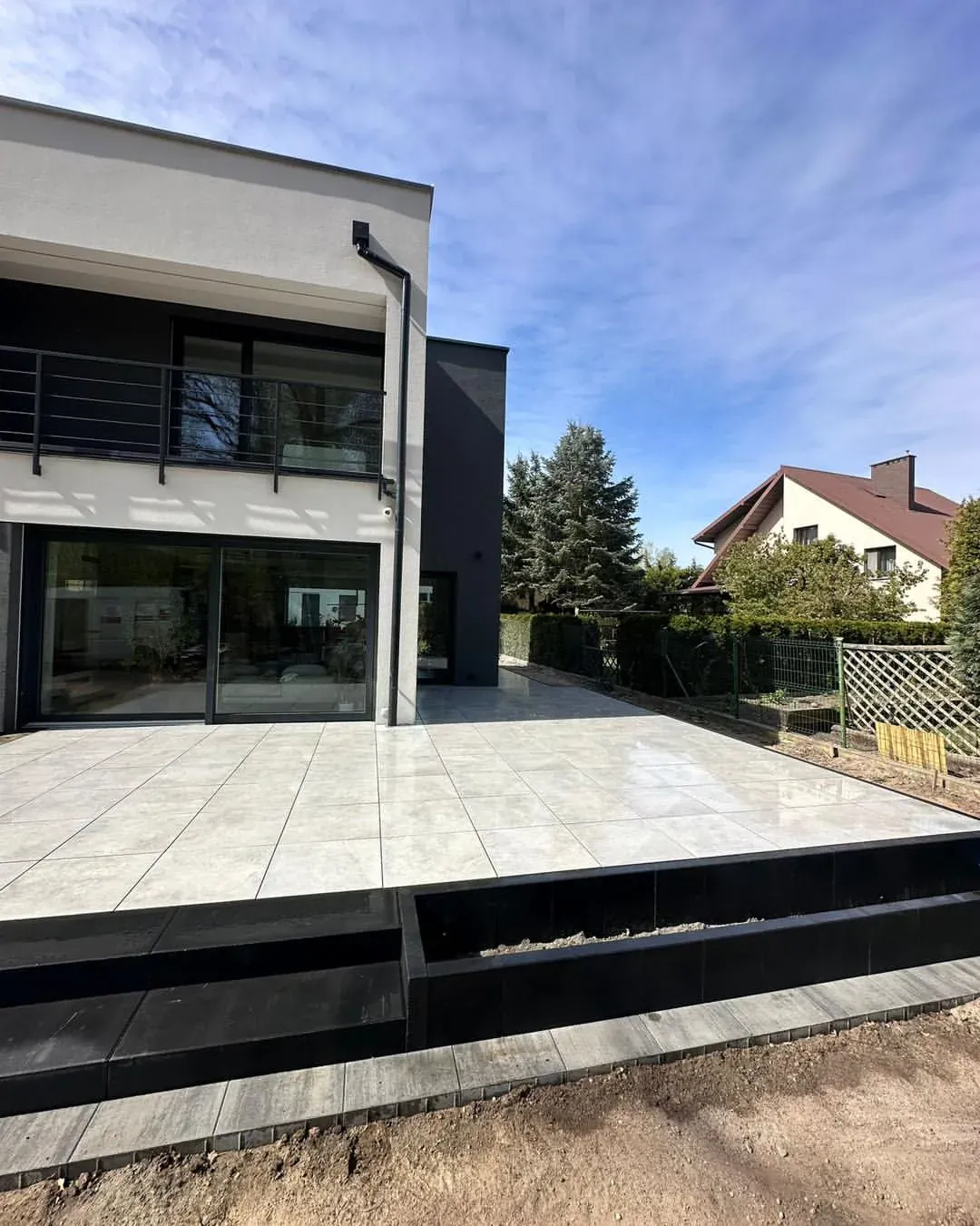 Taras z płyt gresowych 60x60 z cokołem z palisad przy nowoczesnym domu