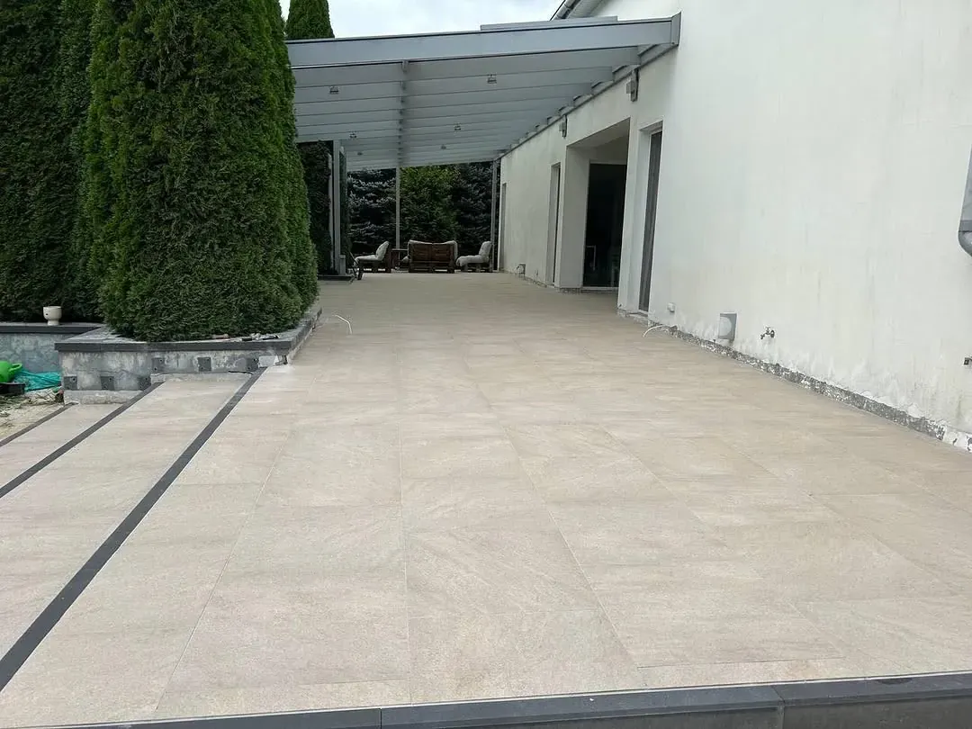 Jasna nawierzchnia z płyt gresowych z ciemnymi pasami pod zadaszeniem tarasu