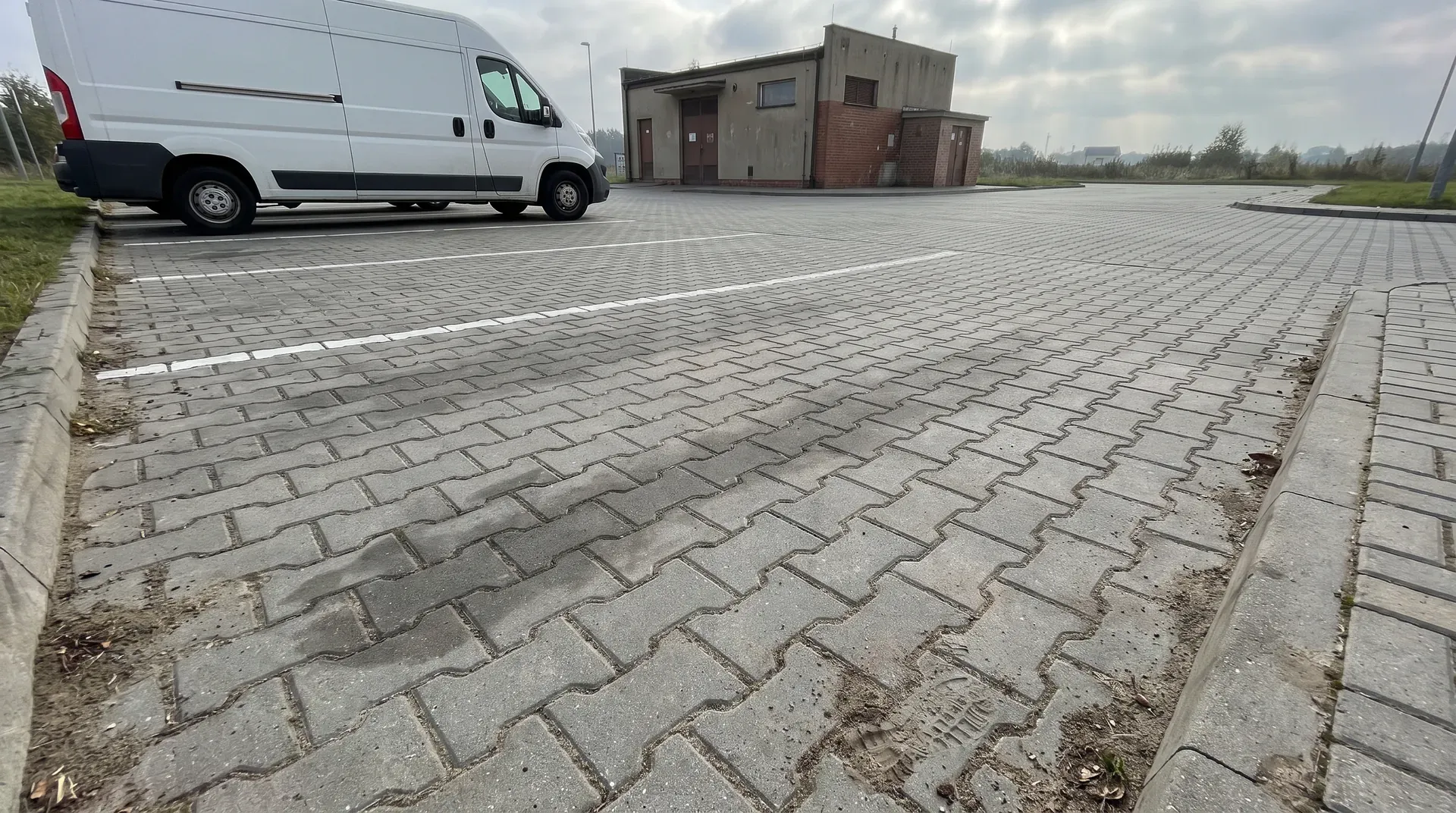 Parking z szarej kostki przy budynku usługowym z wyznaczonymi miejscami postojowymi