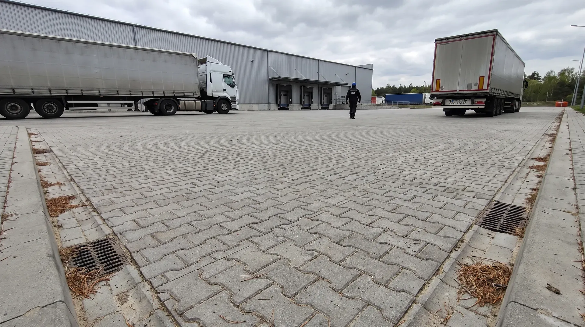Plac manewrowy z grubej kostki przemysłowej przed magazynem z krawężnikami i odwodnieniem