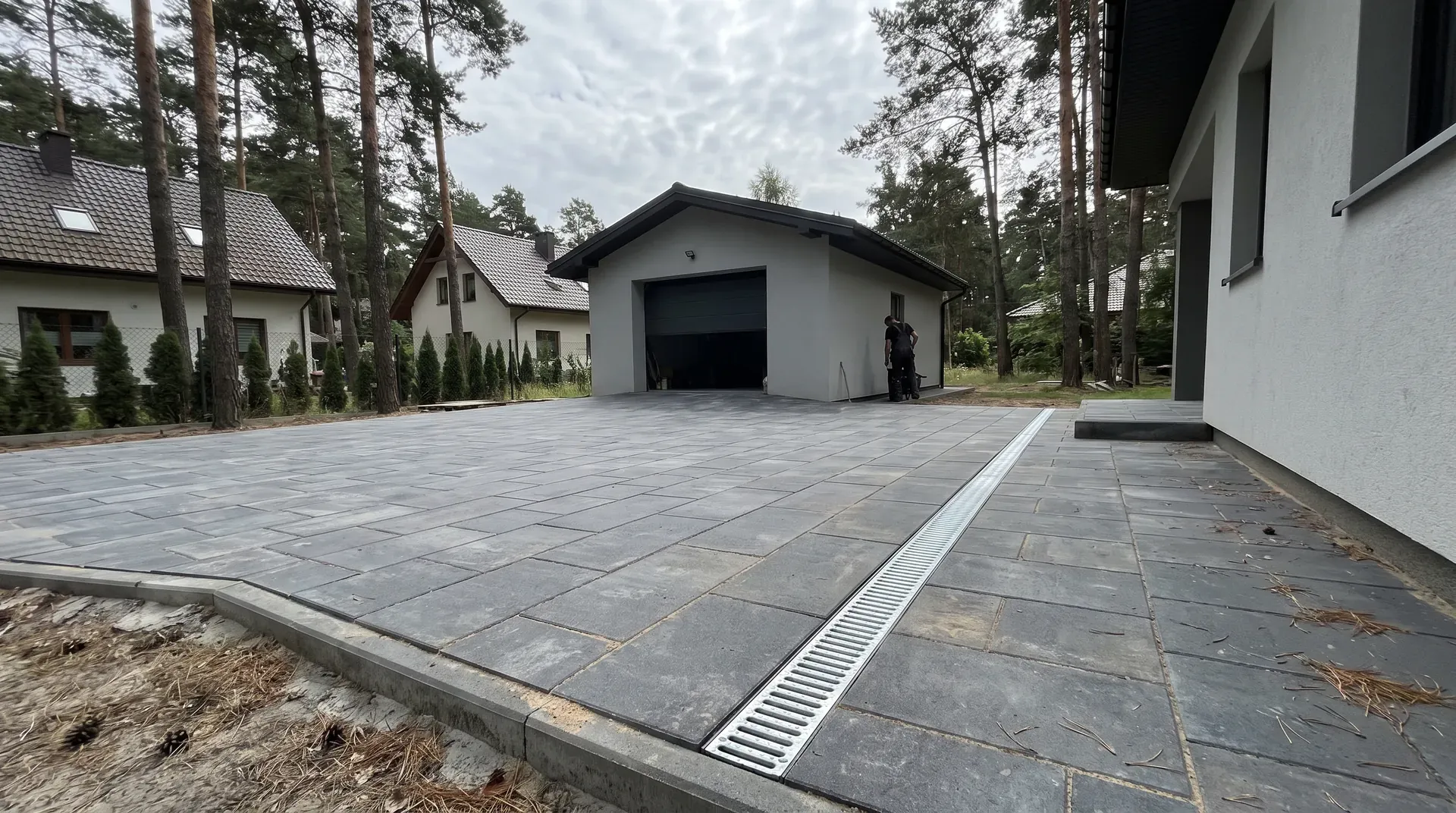 Nowy szary podjazd z kostki betonowej przed garażem wśród sosen w Wawrze